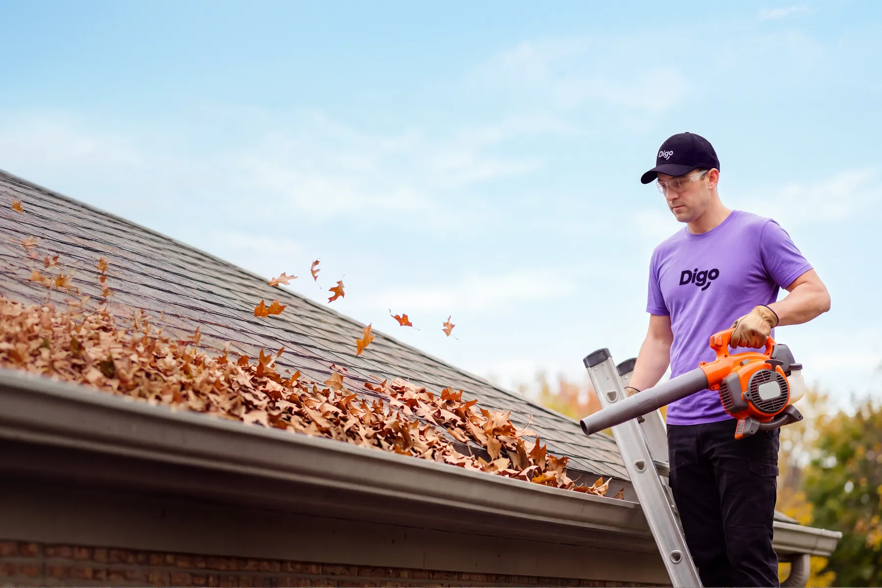 Travailleur Digo en t-shirt violet nettoyant des gouttières remplies de feuilles mortes